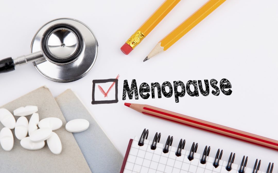 Tabletten liegen auf dem Tisch neben einer Checkliste, auf der Menopause angeahakt ist